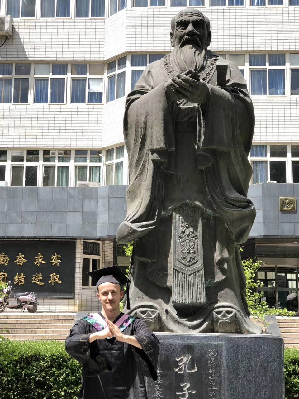 Tony in a graduation gown next to the Confucius statue